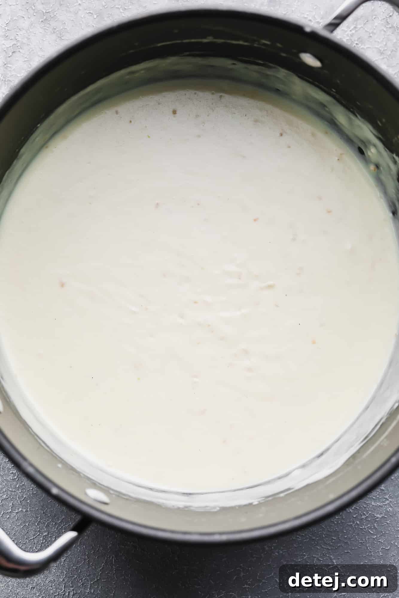 A black pot filled with a luscious white cream sauce, simmering gently.