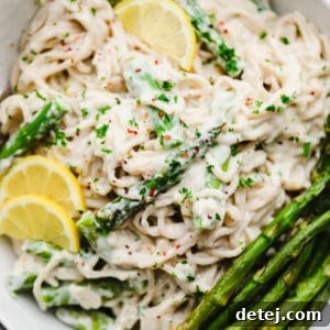 close up on lemon asparagus pasta topped with cooked asparagus and lemon slices in a white bowl.
