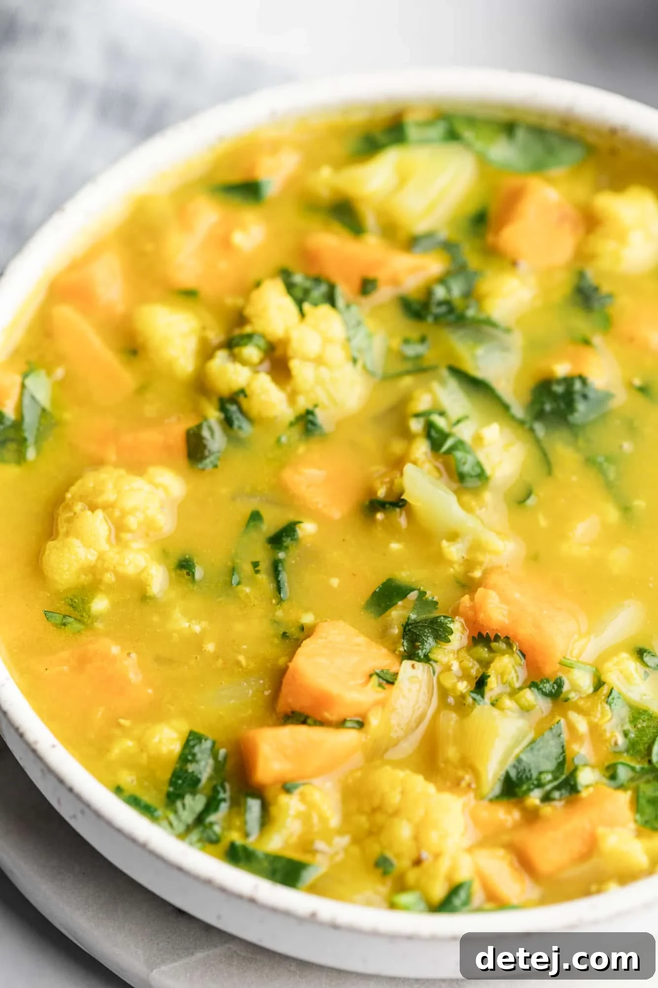 A large white bowl filled with creamy coconut curry lentil soup, garnished with fresh cilantro.