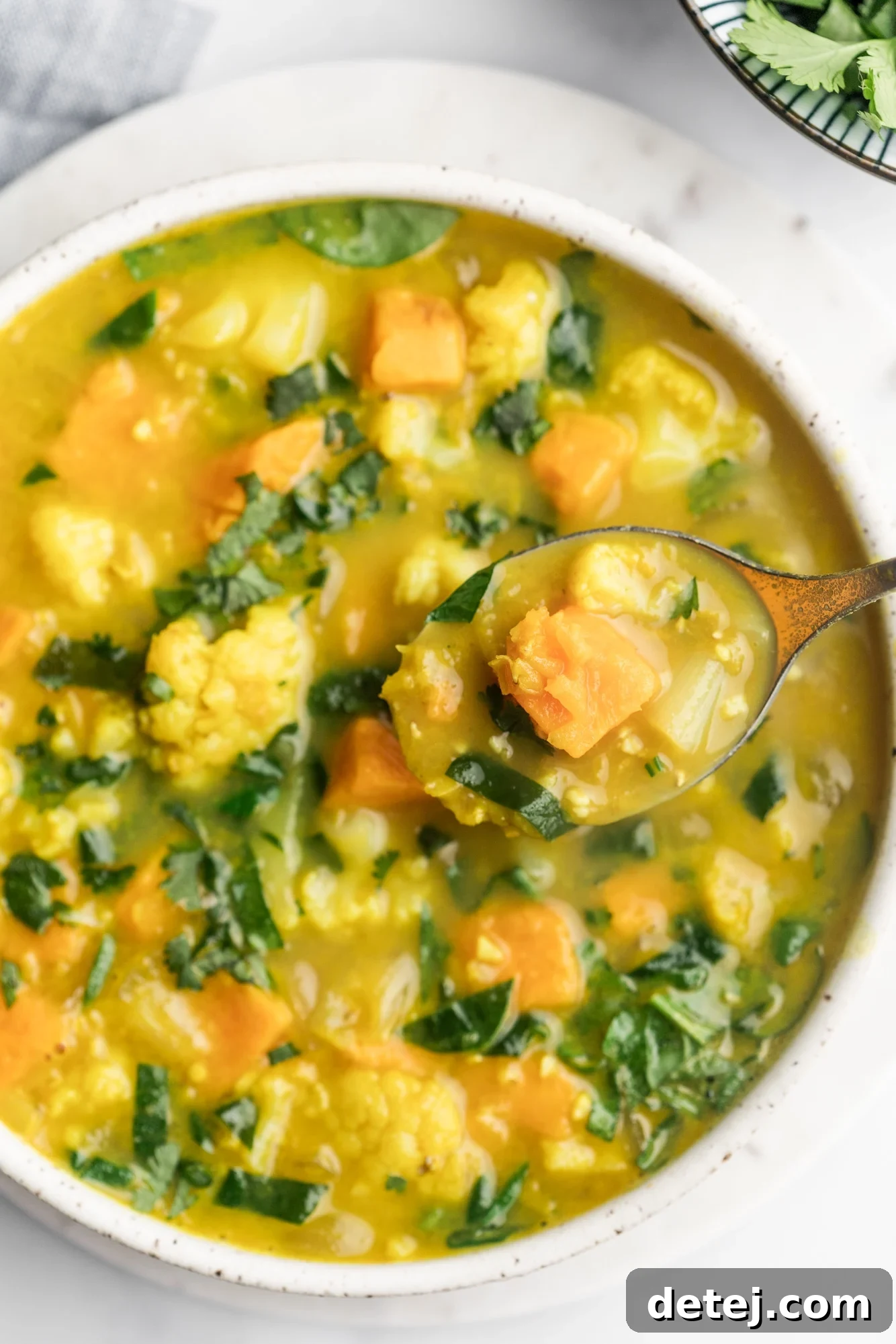 A wooden spoon lifting a scoop of thick coconut curry lentil soup from a large white bowl, showing its rich texture.