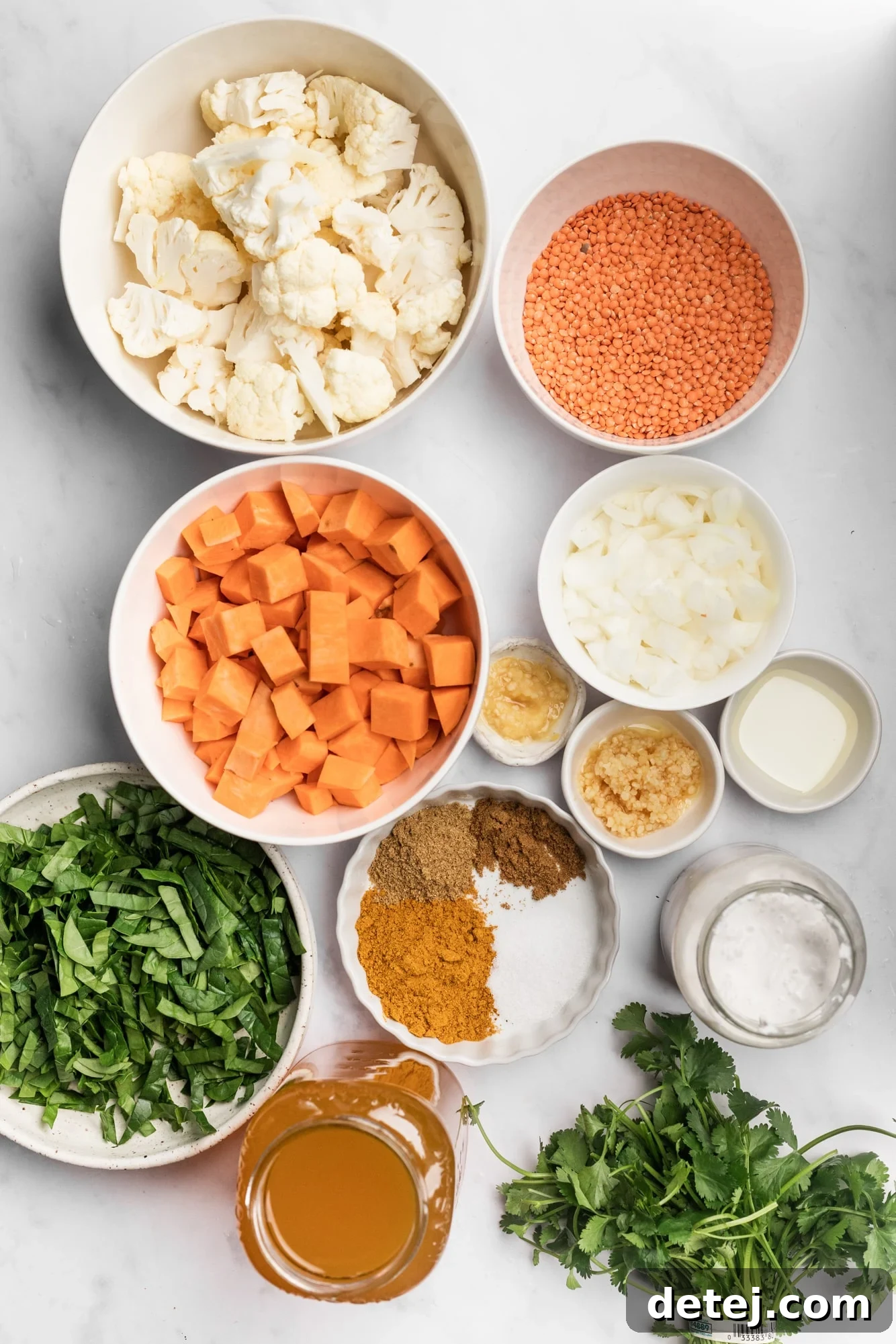 Individual white bowls filled with various ingredients for coconut curry lentil soup, including diced onions, garlic, ginger, spices, lentils, sweet potatoes, and cauliflower.