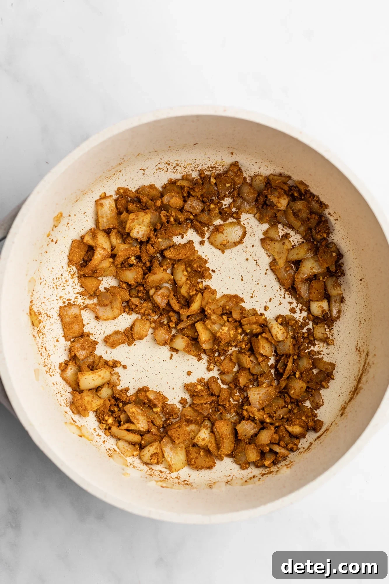 Diced onions, minced garlic, and grated ginger being sautéed with spices in a large white pot.