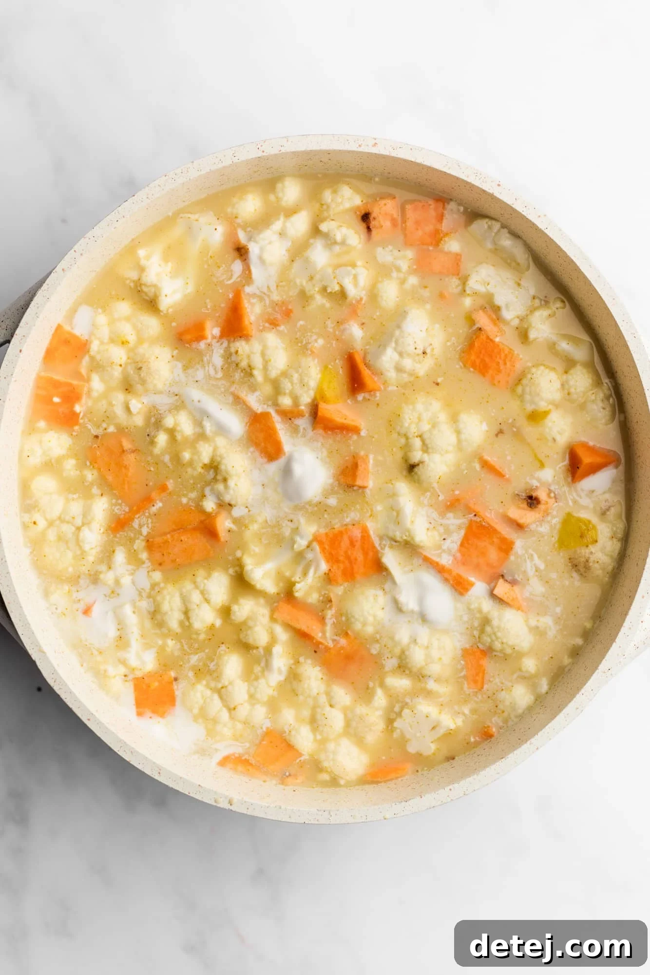Coconut curry lentil soup simmering in a large white pot, with visible lentils, cauliflower, and sweet potatoes.