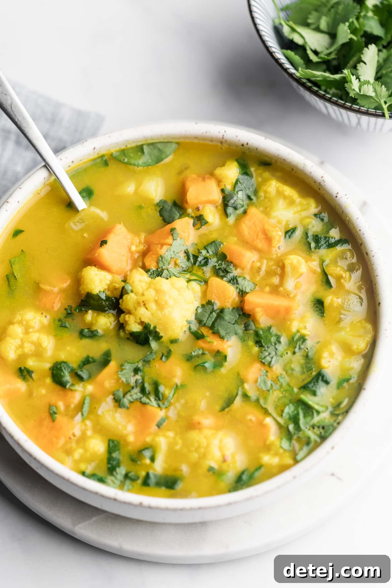 A large white bowl brimming with creamy coconut curry lentil soup, ready to be served.
