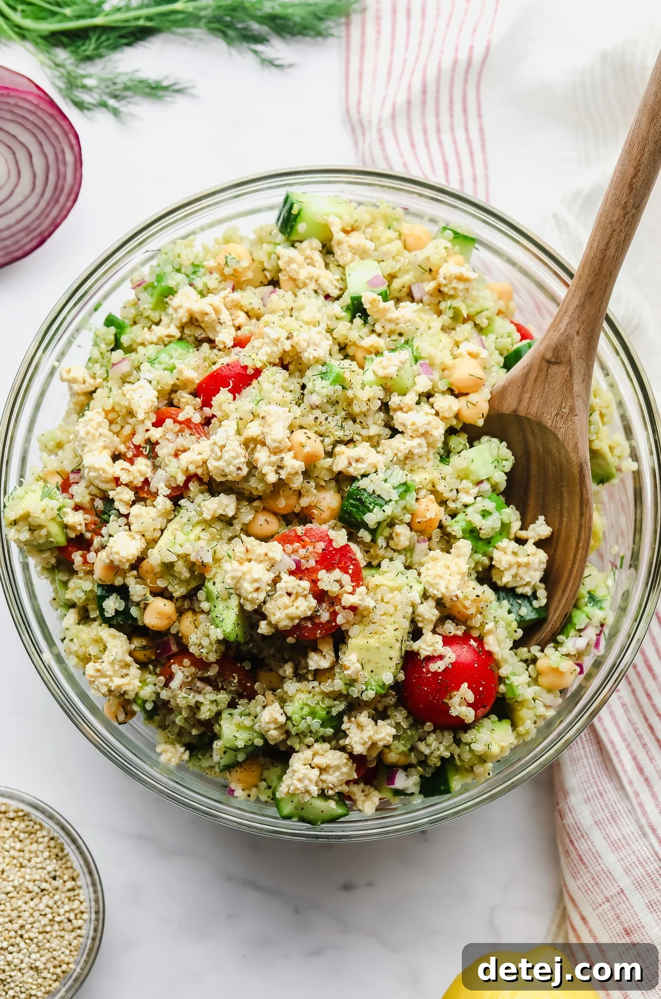stirring a quinoa salad with chickpeas with a wooden spoon in a large glass bowl.