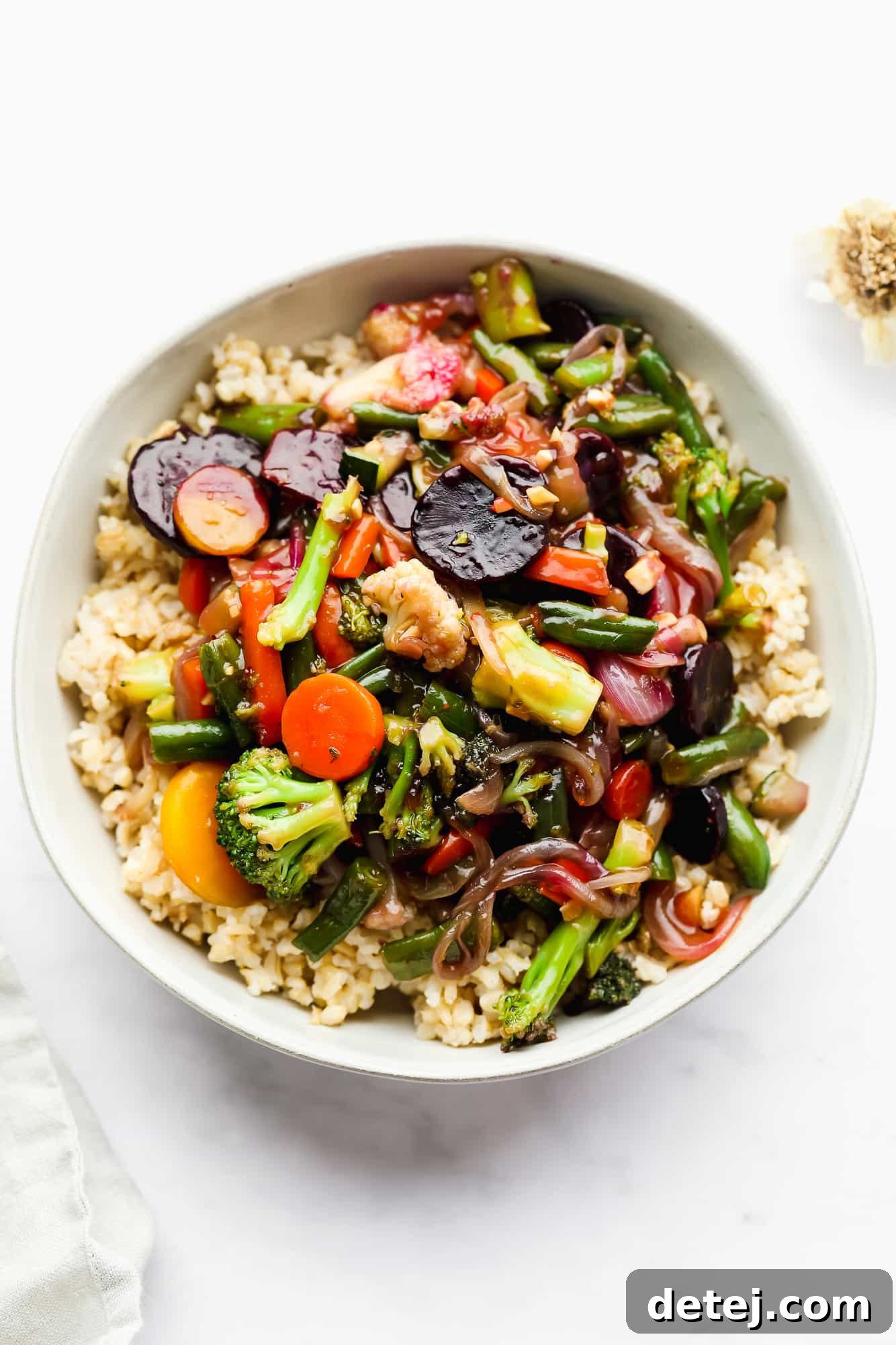 Sauce-covered cooked vegetables served over white rice in a pristine white bowl.