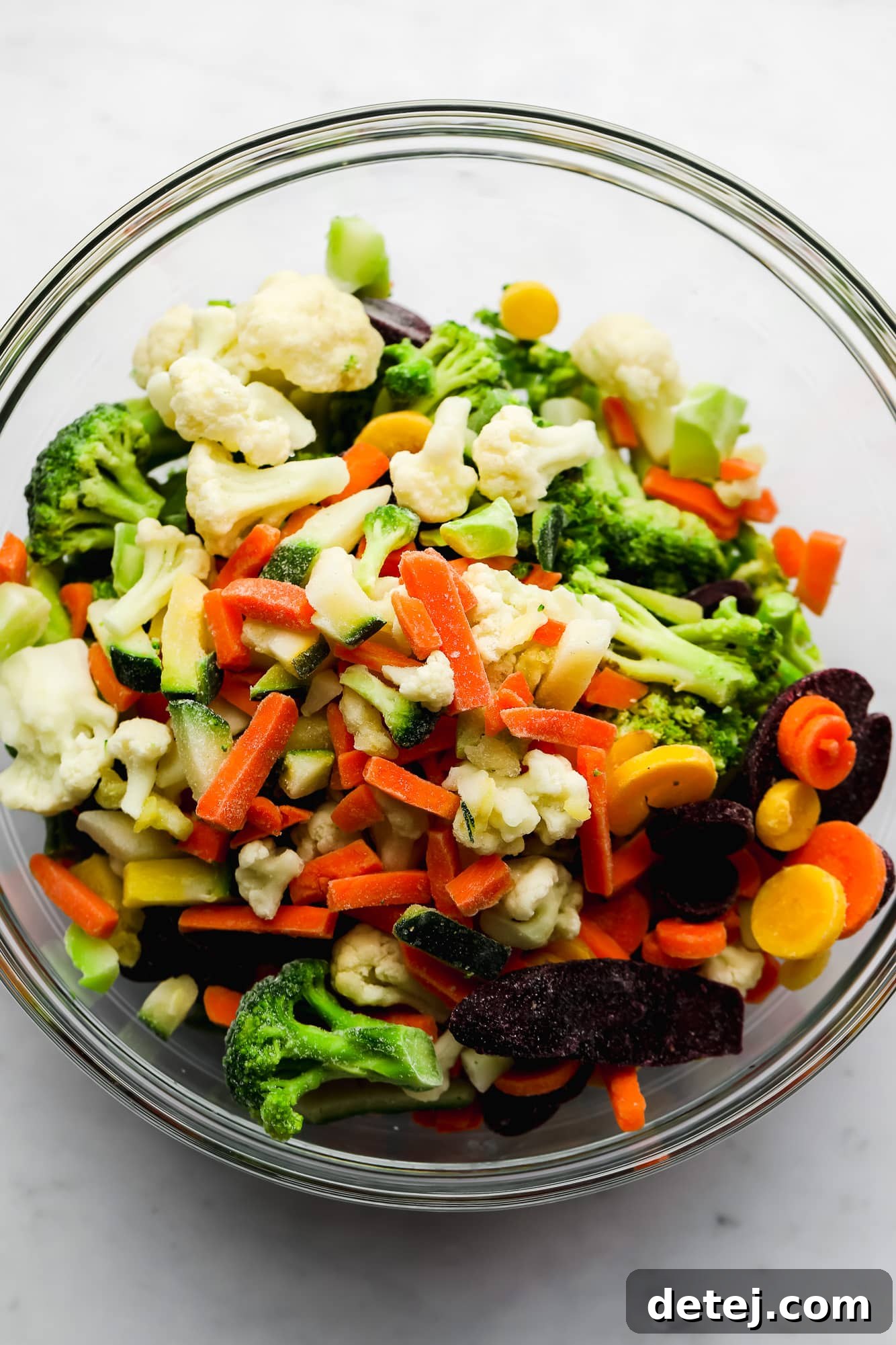 A vibrant medley of assorted frozen vegetables neatly arranged in a clear glass bowl, showcasing their fresh appearance despite being frozen.
