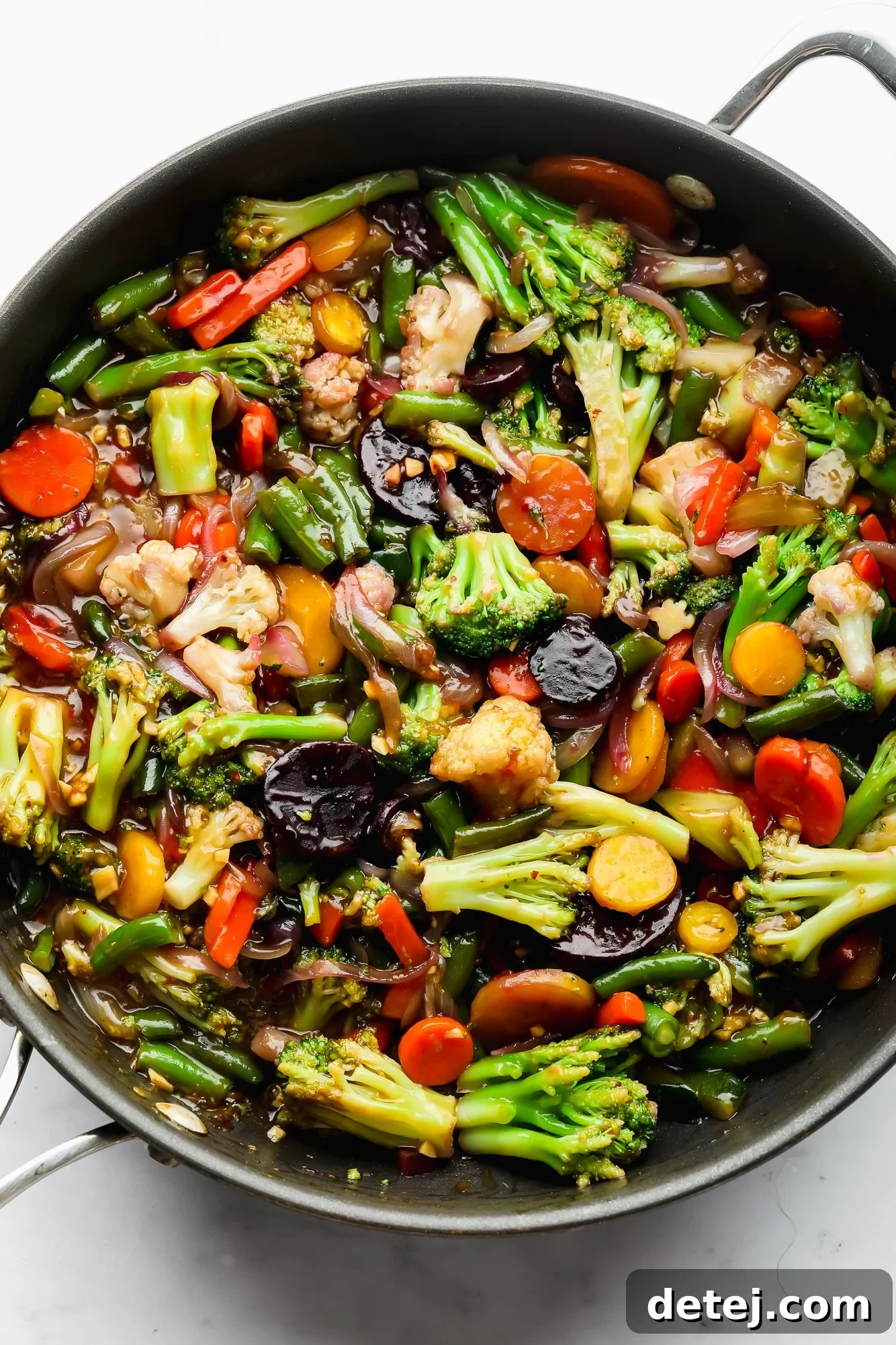 A large black skillet filled with perfectly cooked, sauce-covered vegetables, glistening and ready to serve.
