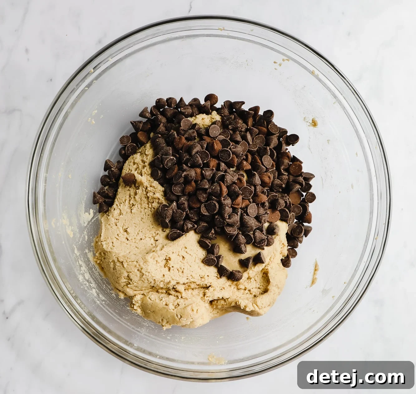 A glass bowl filled with rich, creamy cookie dough, generously studded with glistening vegan chocolate chips.