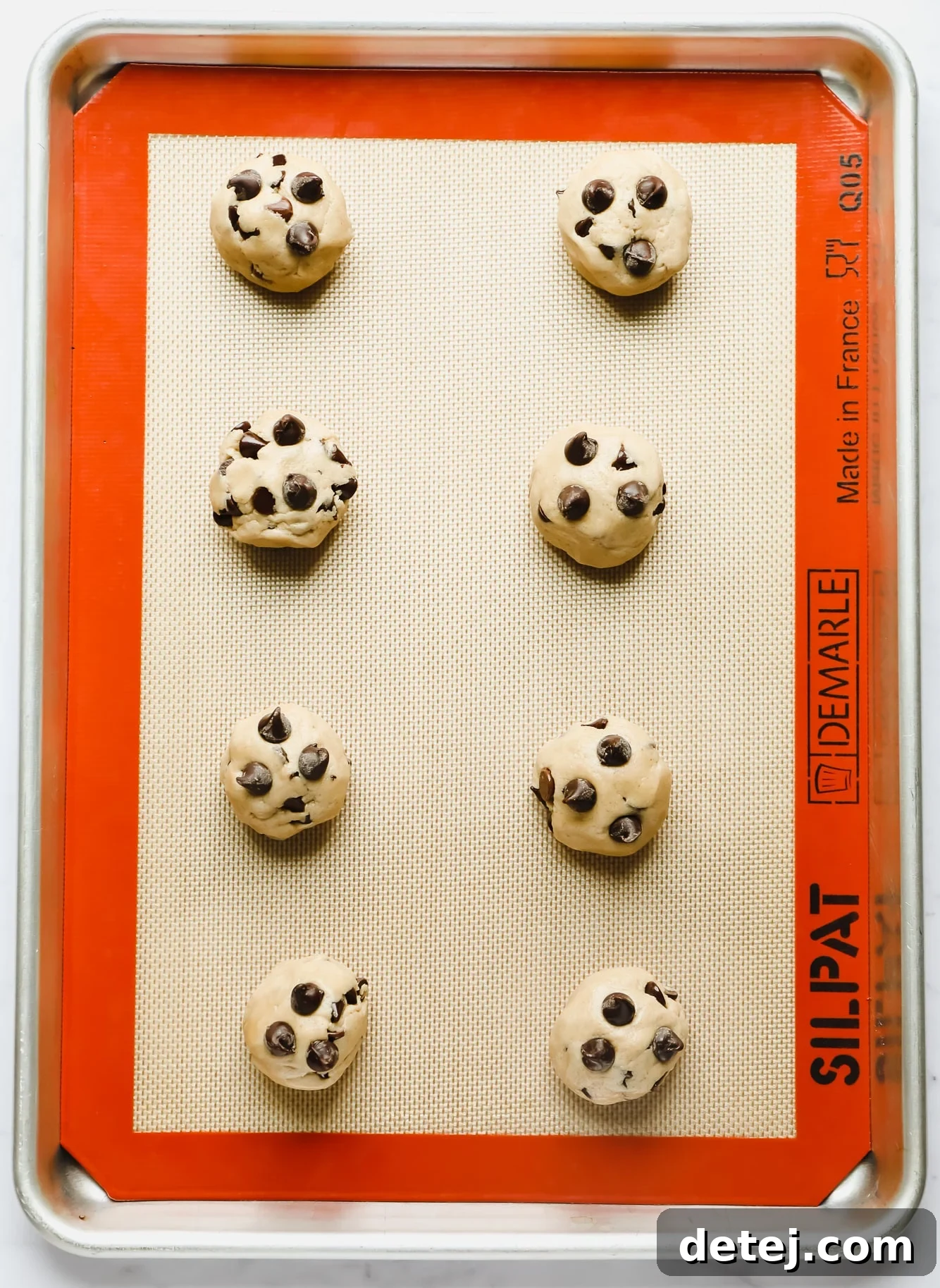 Perfectly portioned balls of vegan gluten-free cookie dough awaiting their bake on a silicone mat-lined pan.