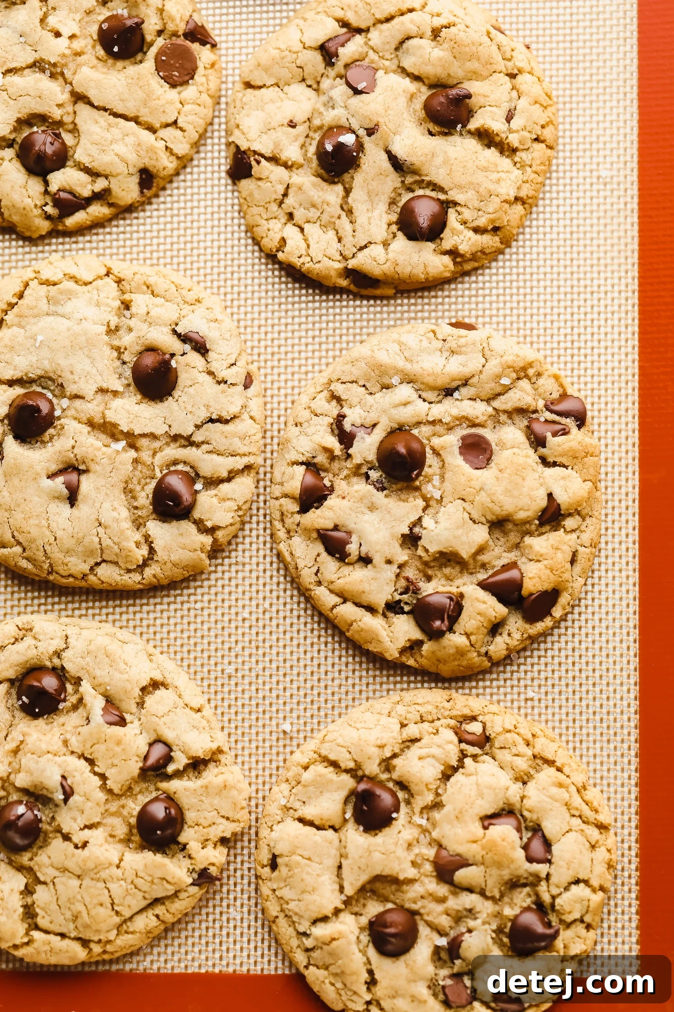 Six golden-brown vegan gluten-free chocolate chip cookies cooling on a silicone mat after baking.