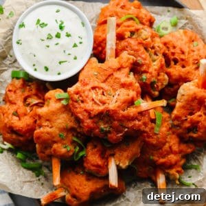 Wingless Wonders 12 A close-up shot of a pile of vegan wings, generously coated in sauce, with a small bowl of creamy white dipping sauce nearby.
