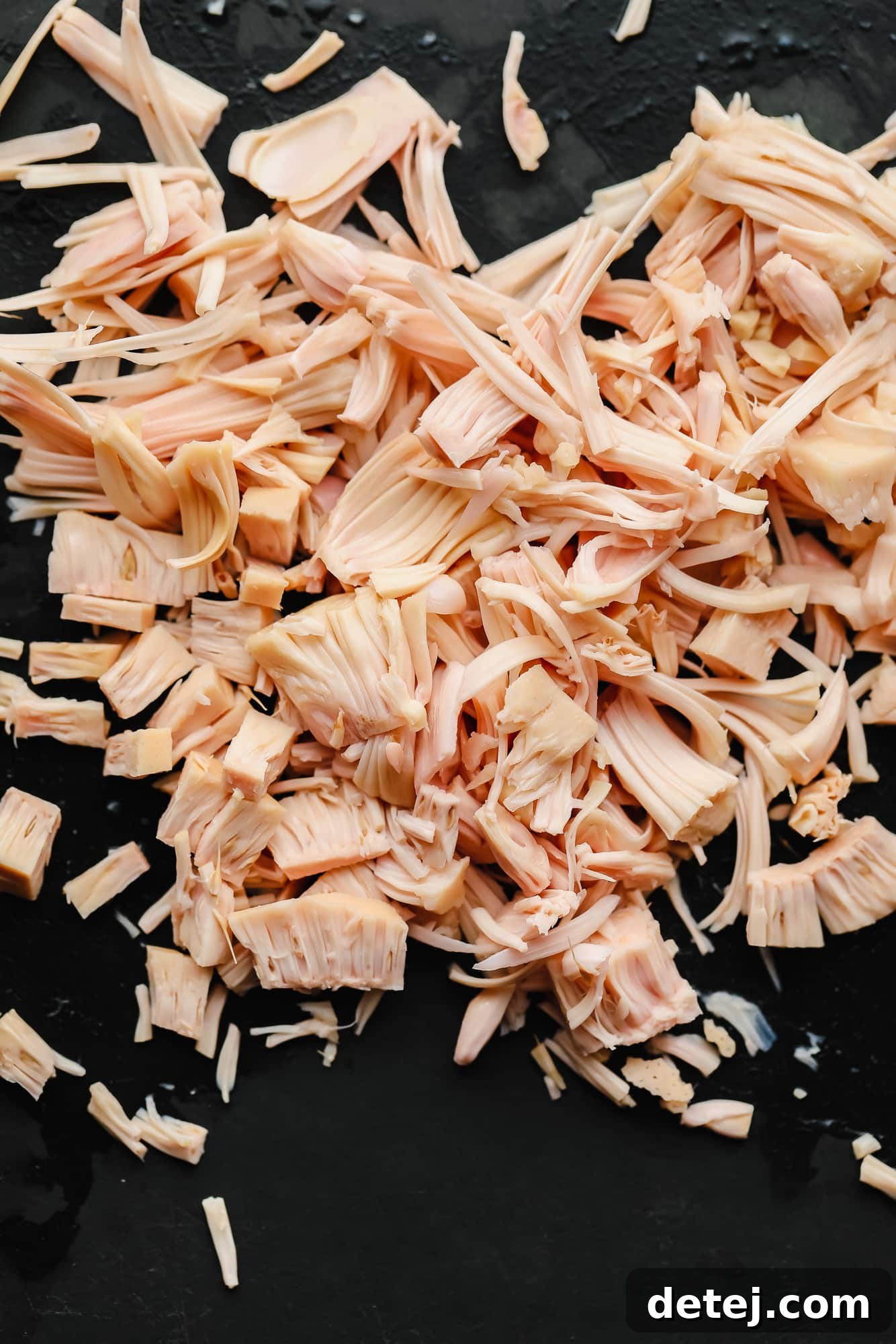 Wingless Wonders 5 Shredded jackfruit, meticulously prepared and laid out on a black cutting board, ready to be incorporated into the vegan wing mixture.