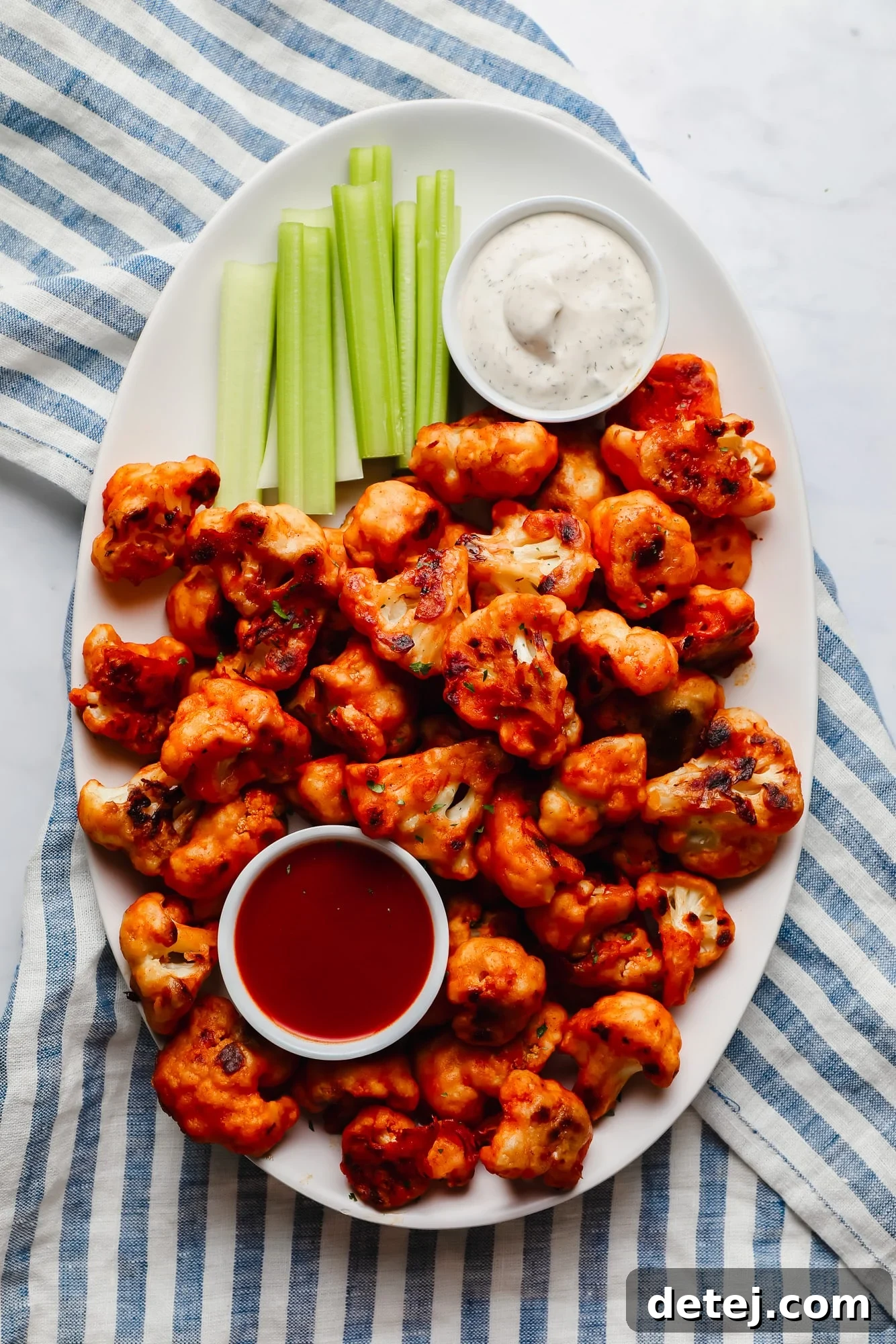 buffalo cauliflower wings, celery sticks, a bowl of ranch dressing, and a bowl of buffalo sauce on a large white platter.
