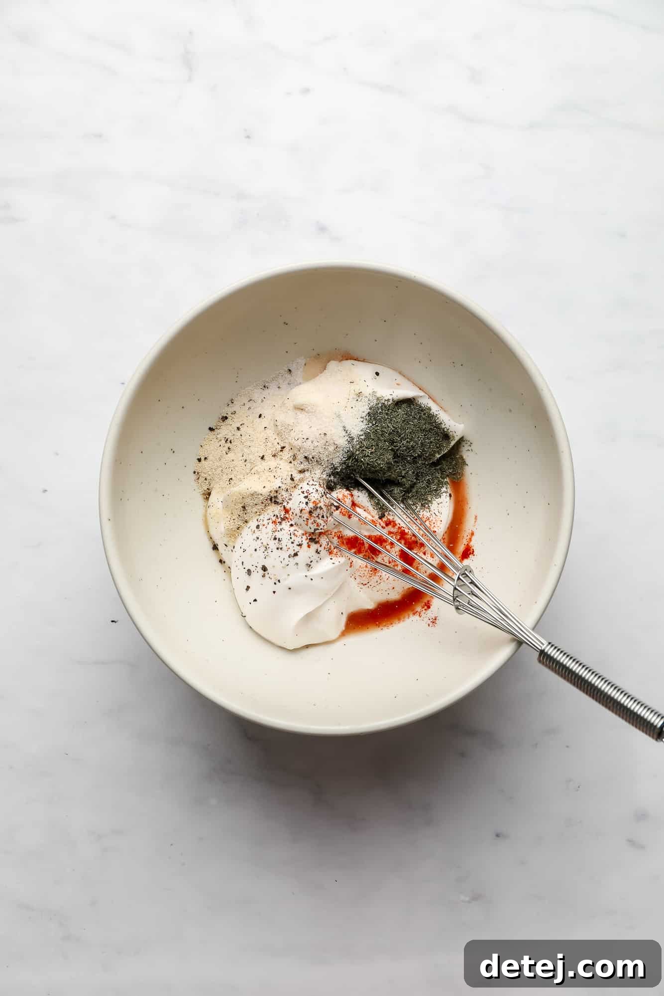 whisking the ingredients for vegan ranch dressing in a white bowl.
