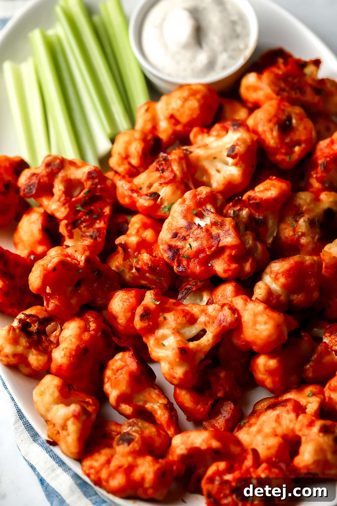 close up on buffalo cauliflower on a white platter with celery sticks and ranch dipping sauce on the side.