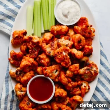 buffalo cauliflower wings, celery sticks, a bowl of ranch dressing, and a bowl of buffalo sauce on a large white platter.