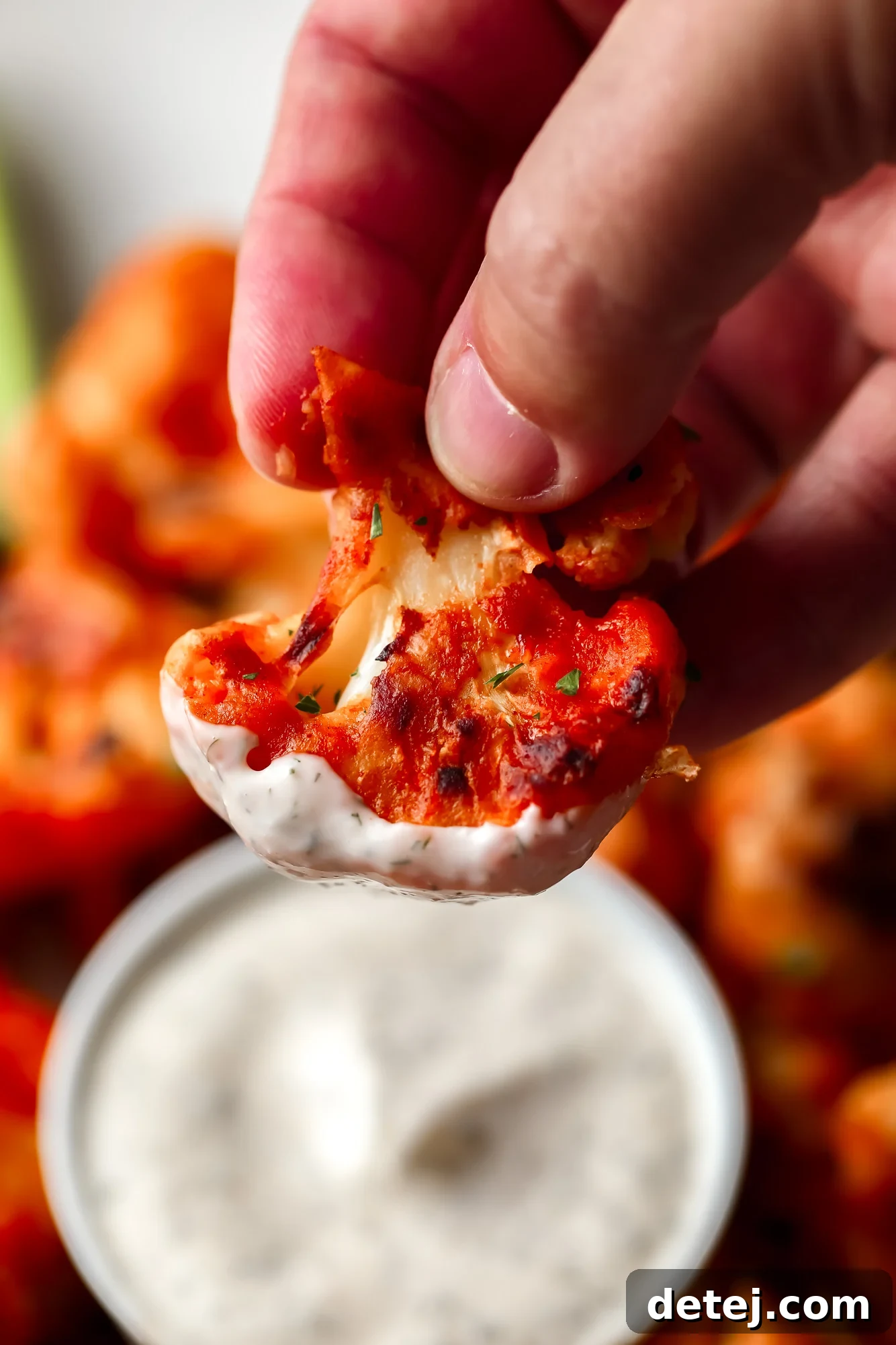 a hand dipping a buffalo cauliflower into vegan ranch dressing.