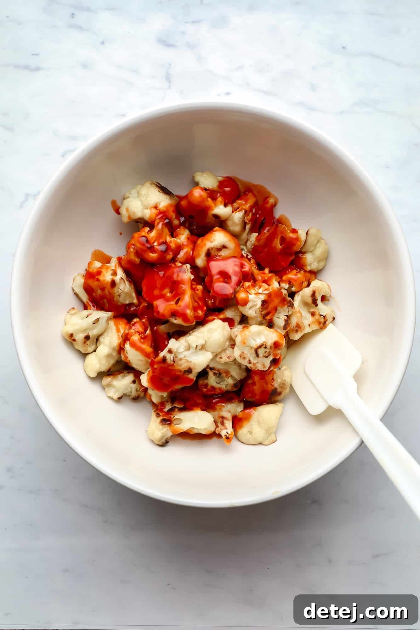 tossing cauliflower wings in buffalo sauce in a white bowl.