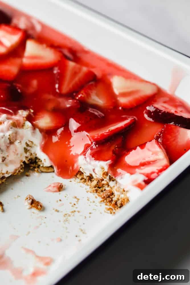 A white baking dish filled with a perfectly layered strawberry pretzel salad, with one square slice elegantly removed to showcase its distinct layers.