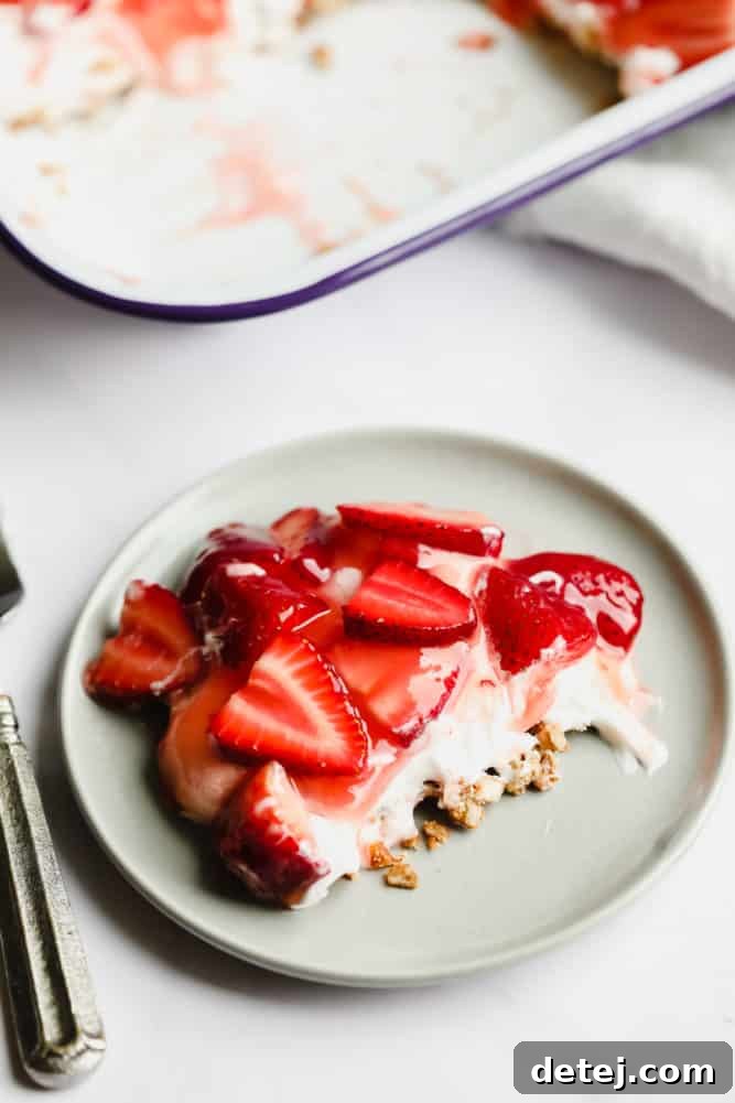 A delectable slice of strawberry pretzel salad served on a grey plate, clearly showing the crunchy pretzel base, the smooth creamy middle, and the vibrant strawberry topping.