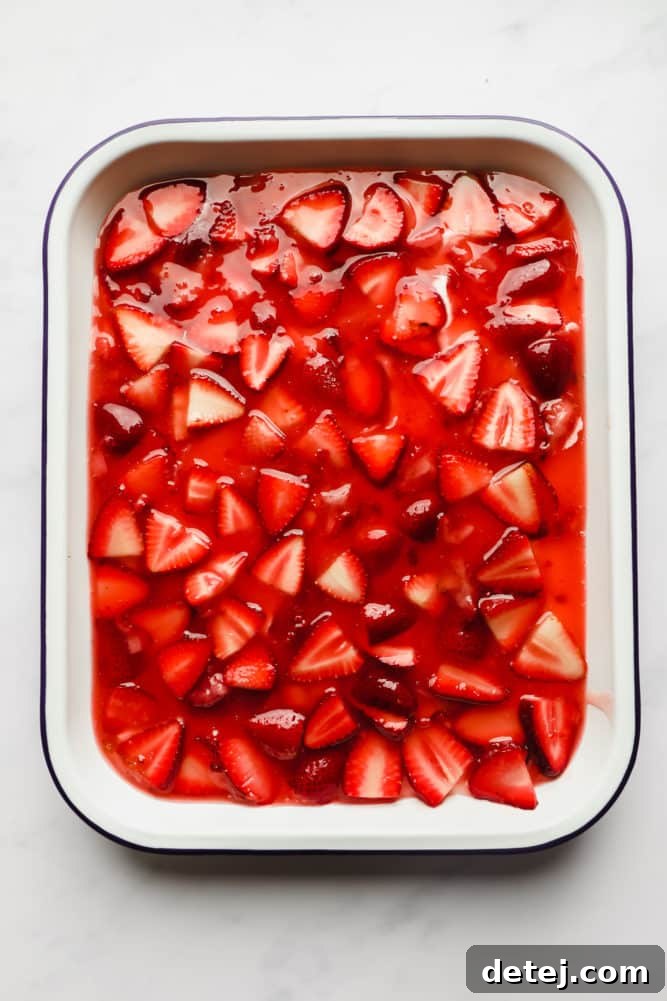 Close-up shot of a white pan with a blue rim, filled with a glossy, vibrant strawberry sauce, showcasing the rich red color and fruit pieces.