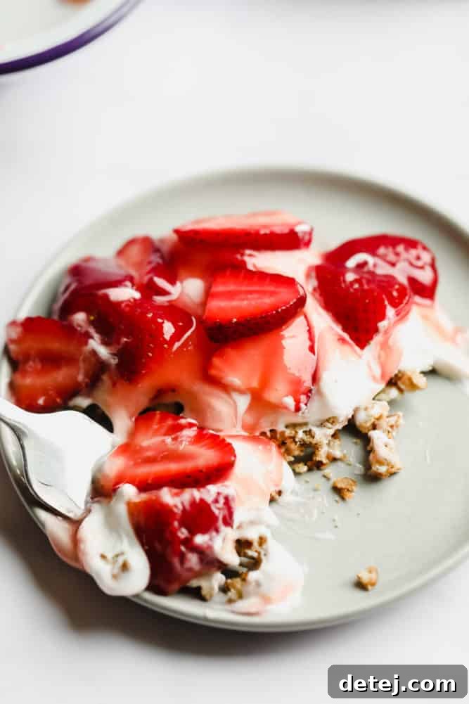 A fork taking a delicious bite out of a slice of strawberry pretzel salad, showing all three perfect layers and the textural contrast.