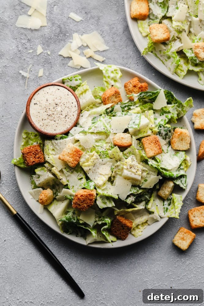 Two plates of a vibrant vegan Caesar salad on a grey background, showcasing fresh ingredients.