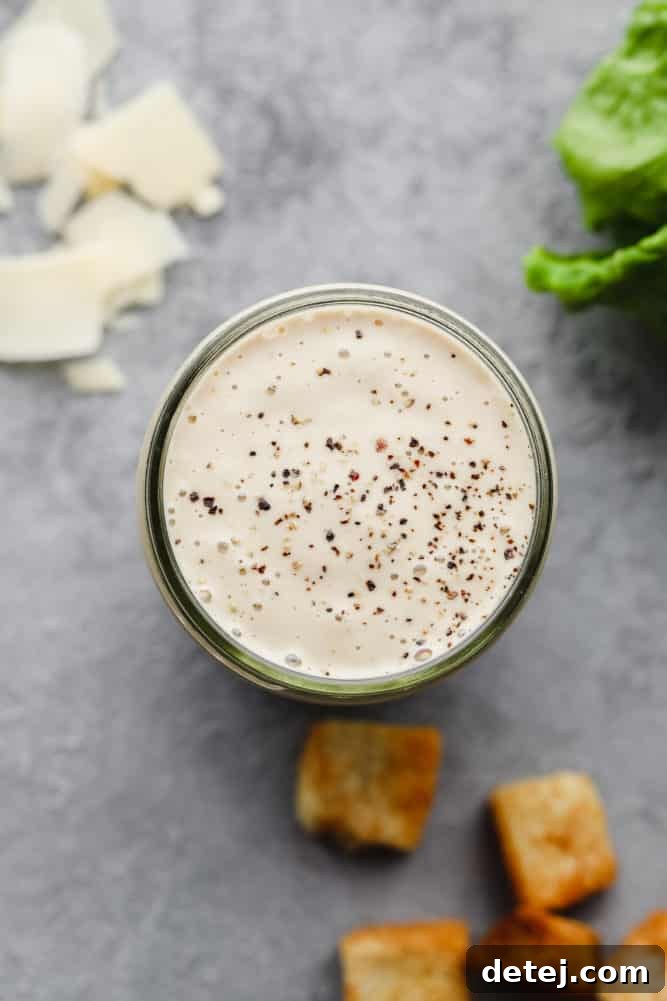 Creamy white vegan Caesar dressing with black pepper in a glass dish on a grey background.
