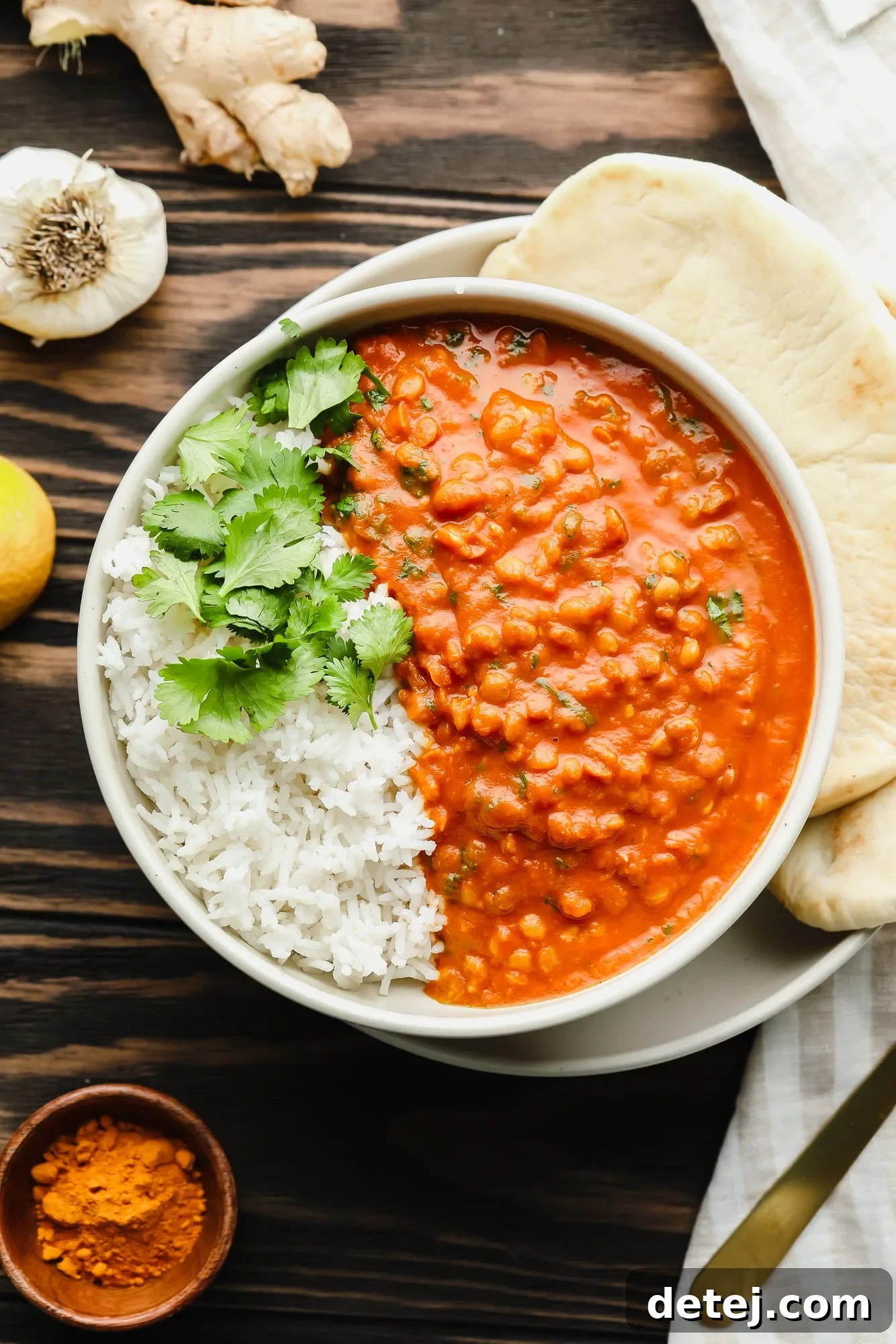 A delicious bowl of lentil curry with white rice and fresh cilantro, served with a side of naan bread.