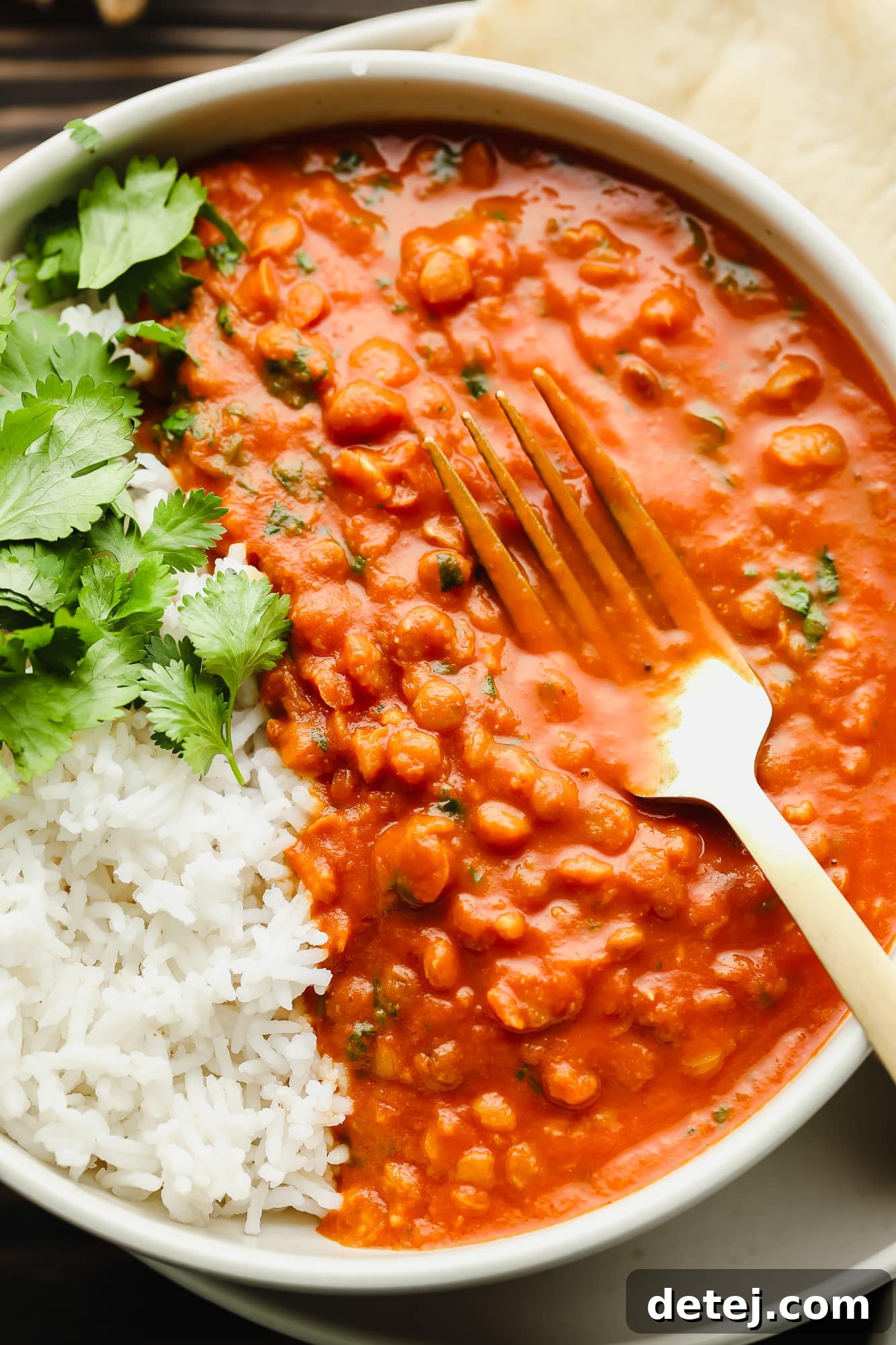 A fork piercing into a hearty bowl of lentil curry with white rice, ready to be enjoyed.