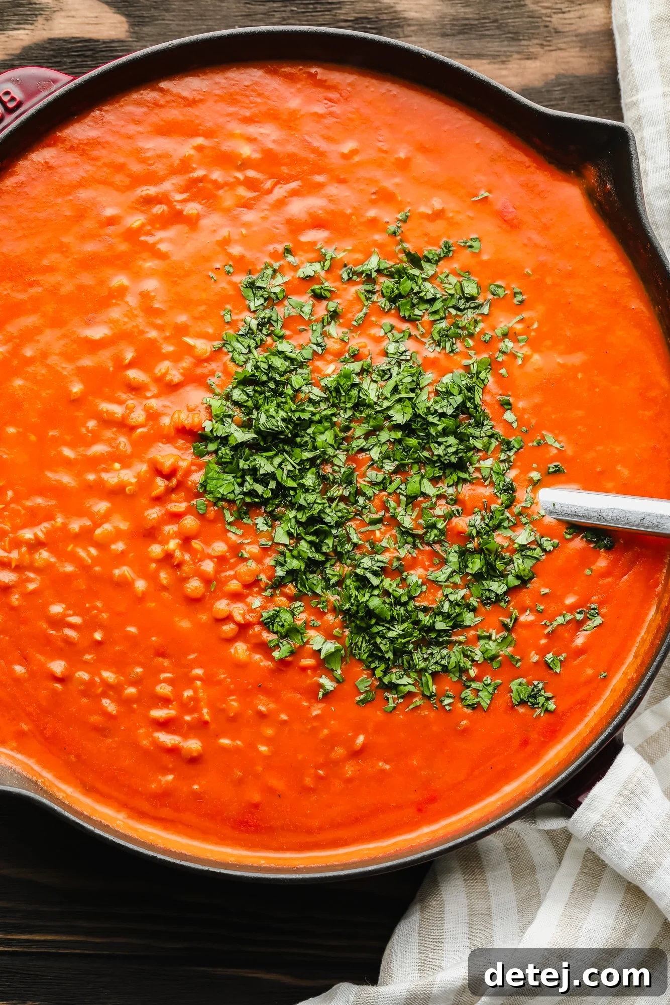 A large black pot filled with rich lentil curry, generously topped with fresh chopped cilantro leaves.