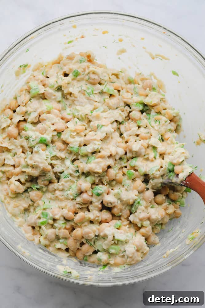 A close-up of a bowl filled with creamy, vibrant green chickpea salad, perfectly mashed and mixed with fresh dill and green onions, ready to be served or stored.