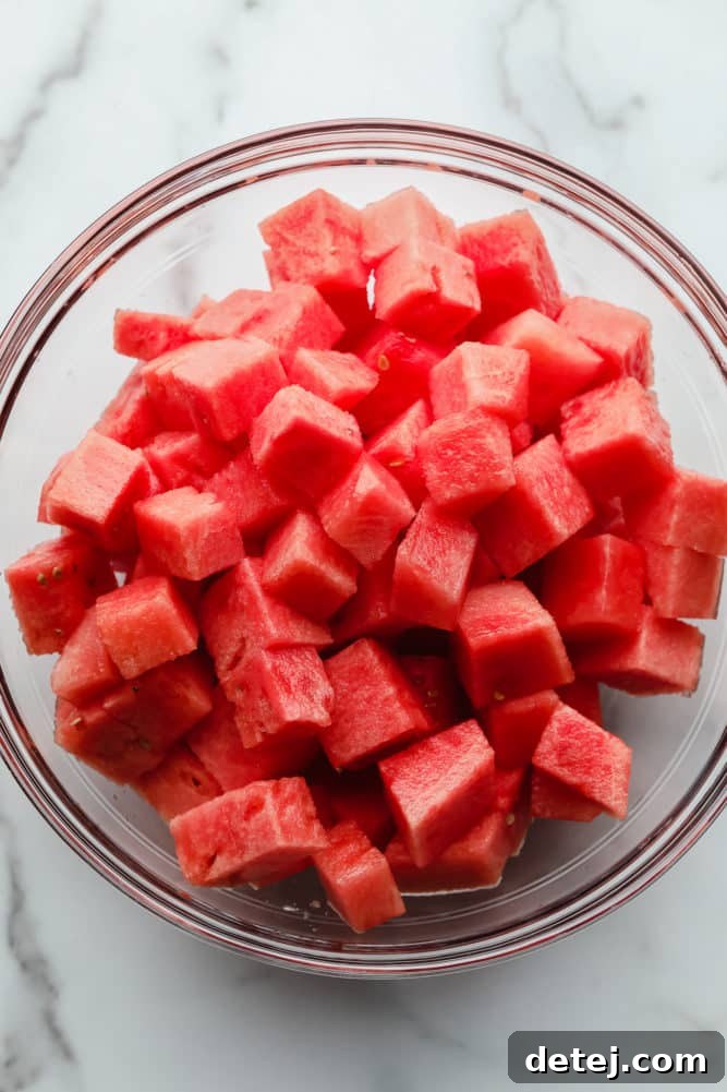 A pristine glass bowl of perfectly cubed watermelon, vibrant and ready for dressing, set against a classic marble background.