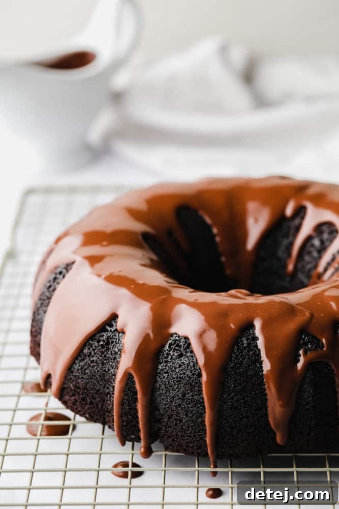 Freshly baked vegan chocolate bundt cake cooling on a rack, drizzled with glossy chocolate ganache