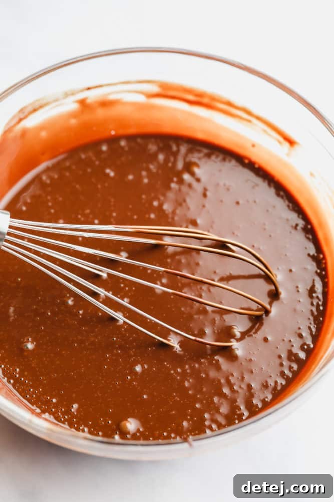 Smooth chocolate ganache in a bowl with a whisk, showing perfect consistency