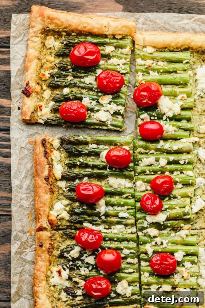 Sliced asparagus puff pastry tart with whole cherry tomatoes, perfectly baked to golden perfection on a rustic wooden board.