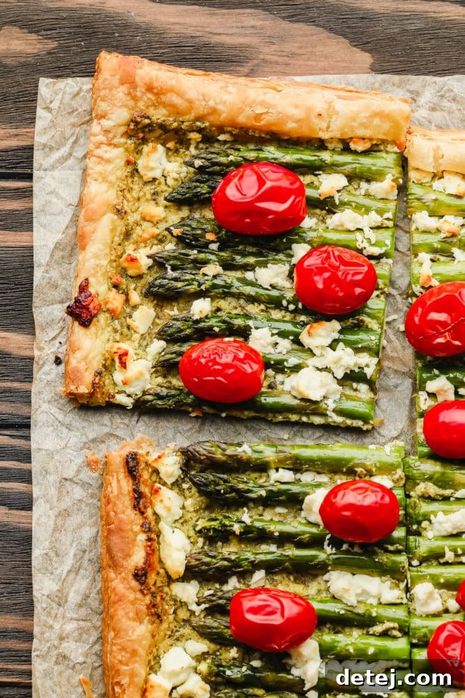 Close-up of a cut puff pastry tart featuring tender asparagus spears and vibrant tomatoes on a warm wooden background.