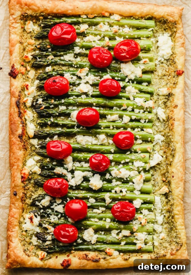 Whole baked asparagus puff pastry tart on parchment paper, adorned with golden crust and melted vegan feta, ready to be cut.