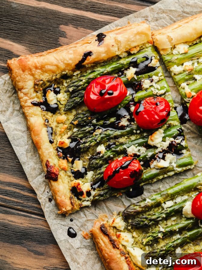 A square slice of baked asparagus puff pastry tart, elegantly drizzled with balsamic glaze, on a white plate, showcasing its flaky layers.