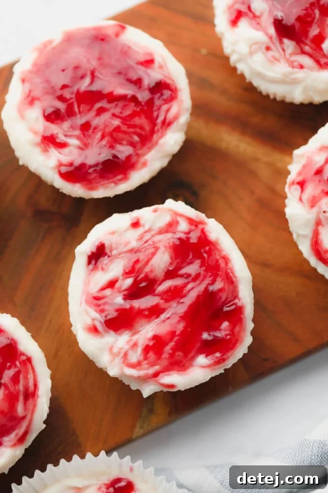 Close-up of creamy cheesecake bites with vibrant raspberry jam swirls on a cutting board, showcasing the beautiful marbling and tempting texture.