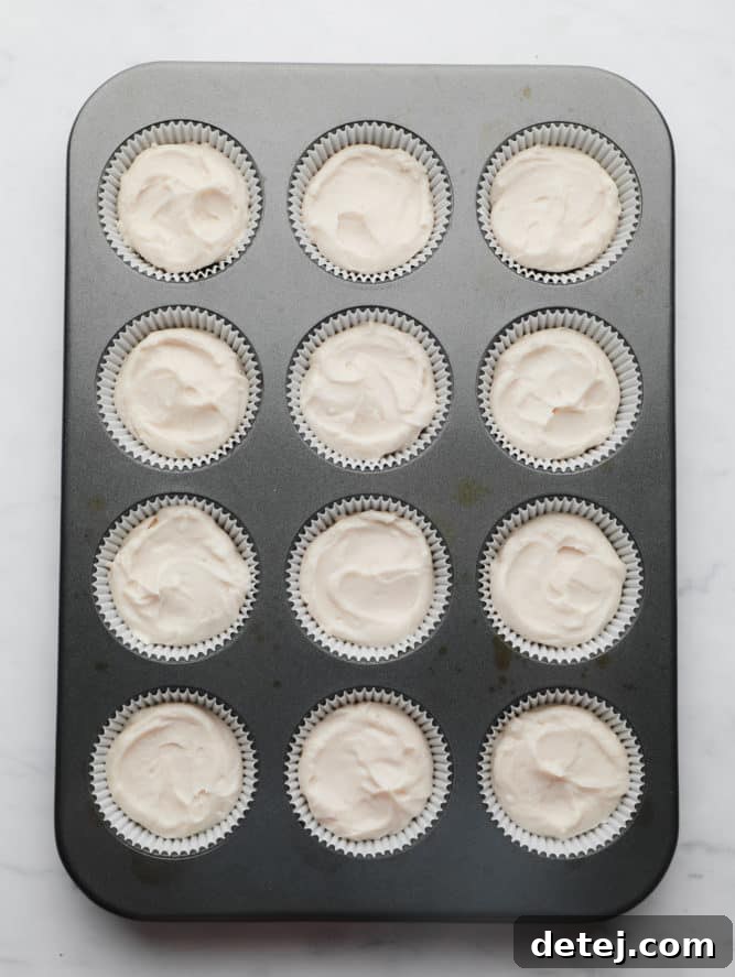 A muffin pan with twelve paper liners, each filled with a generous dollop of creamy white cheesecake filling, perfectly spread over the cookie crust.