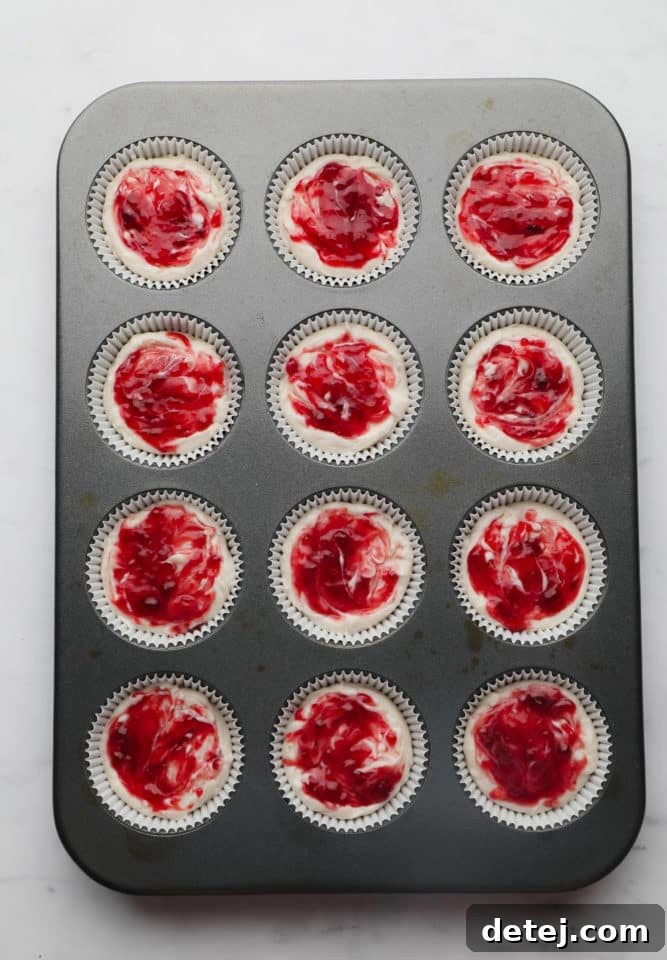 Freshly chilled mini cheesecakes, each featuring a vibrant raspberry swirl, still nestled in their muffin pan, ready to be enjoyed as a cool, refreshing treat.