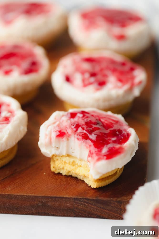 A close-up shot of a single no-bake mini cheesecake on a wooden cutting board, with a bite taken out, revealing its creamy white interior and the contrasting cookie crust.