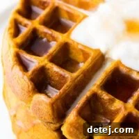 A very close-up side shot of crispy, golden-brown vegan pumpkin waffles, highlighting their perfect texture.