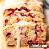 A square image of a perfectly baked loaf of cranberry orange bread, showcasing its golden crust and fruity interior.