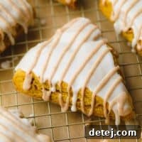 A delicious triangle-shaped vegan pumpkin scone with white and tan glaze, cooling on a rack, ready to be enjoyed.