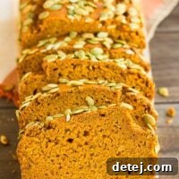 A perfectly sliced vegan pumpkin loaf, showcasing its moist interior, set against a rustic brown wood background with an orange towel.