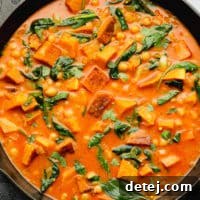 Wilted spinach, perfectly cubed butternut squash, and tender chickpeas simmered in a rich, vibrant orange curry liquid in a black skillet.