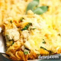 A square image of a bubbling pumpkin pasta bake with almond ricotta, fresh out of the oven in a baking dish.